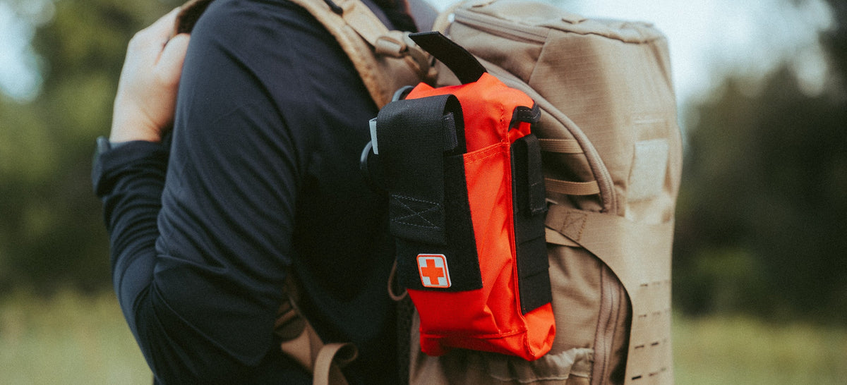 Red D.A.R.K. Trauma Kit mounted on a coyote backpack outdoors