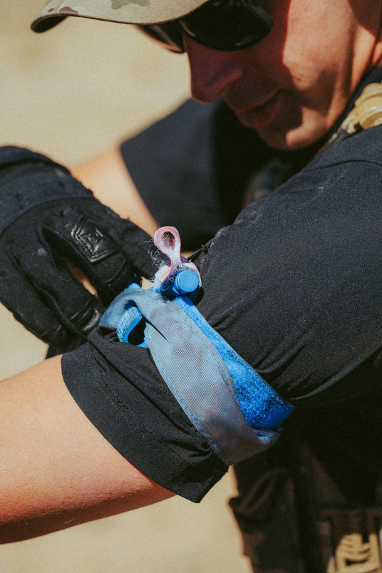 Student applying a training tourniquet to a partner's arm outdoors