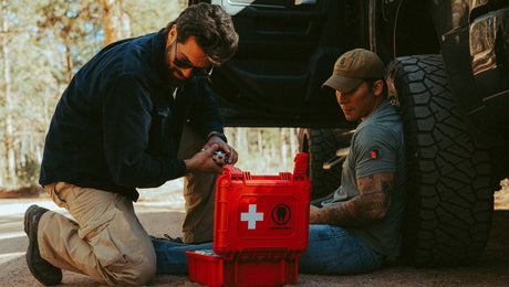 Man rendering aid to another man beside a truck with the HARD Case first aid kit open
