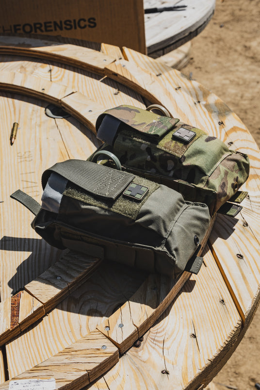 Ranger green and multicam D.A.R.K. Trauma Kits on a wooden spool at the range