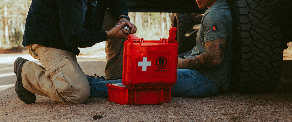 Man rendering aid to another man beside a truck with the HARD Case first aid kit open