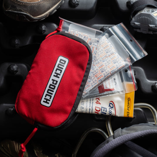 Ouch Pouch first aid kit with bandages, gauze, and dressing packs spread beside the red pouch