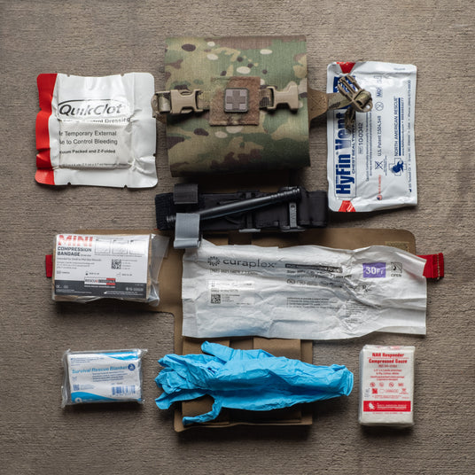 S.P.E.A.R. trauma kit contents including tourniquet, hemostatic dressing, chest seals, and compression bandage around the rolled kit