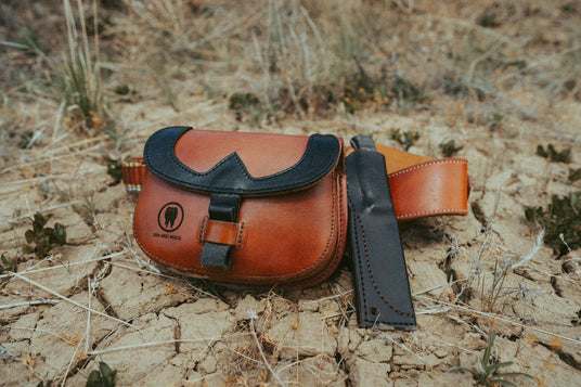 Frontier T.R.A.I.L. leather trauma kit beside a knife sheath on desert ground