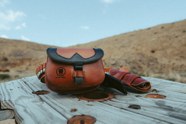 Frontier T.R.A.I.L. leather trauma kit staged on weathered wood with a cartridge belt